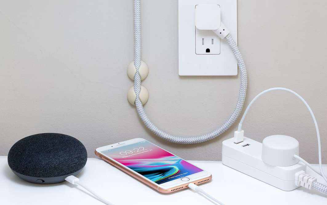A photo of a Google Nest, an iPhone and a smart power strip on a table in front of a power outlet.